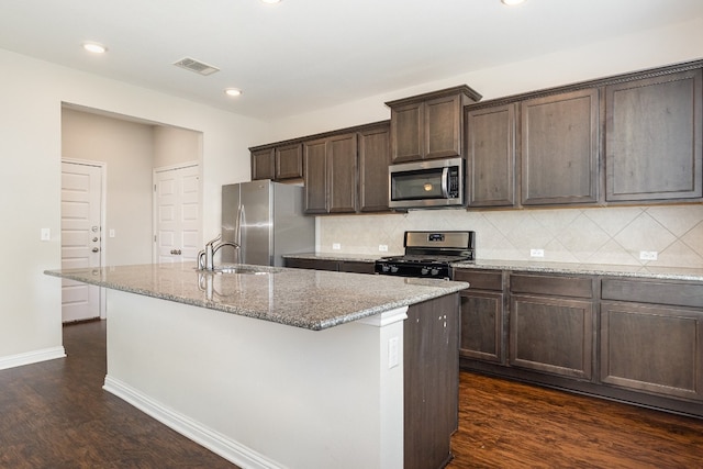 kitchen with tasteful backsplash, dark hardwood / wood-style flooring, sink, appliances with stainless steel finishes, and a center island with sink