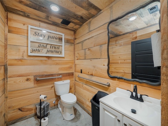 bathroom with wood walls, concrete flooring, vanity, and toilet