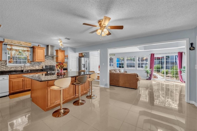 kitchen with stainless steel appliances, a kitchen island, a healthy amount of sunlight, and wall chimney range hood