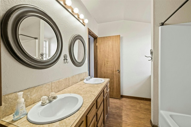 full bath featuring a sink, wood finished floors, double vanity, and vaulted ceiling