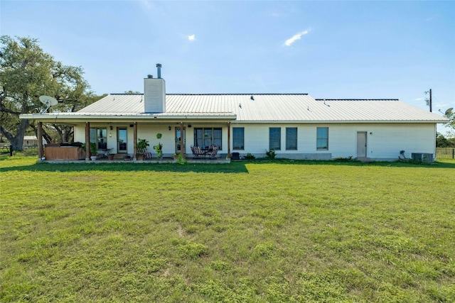 rear view of property with a chimney, a hot tub, a yard, and metal roof