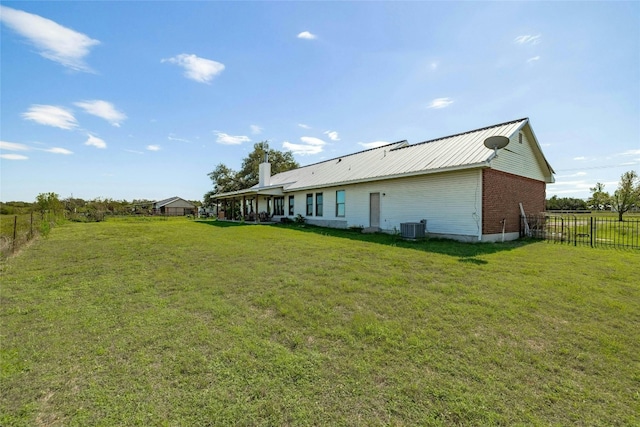 rear view of property featuring cooling unit, metal roof, a yard, and fence