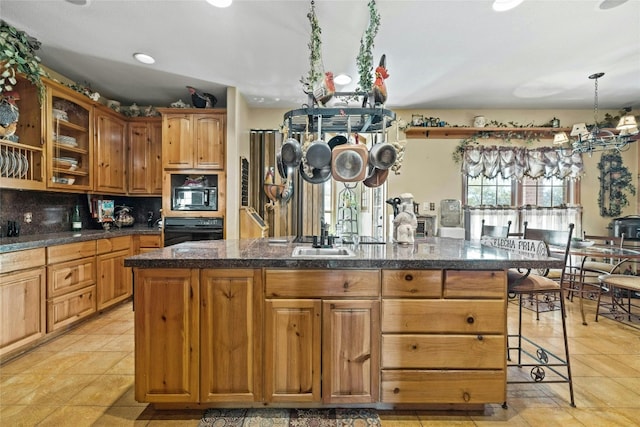 kitchen featuring dark countertops, tasteful backsplash, a center island, black appliances, and a sink