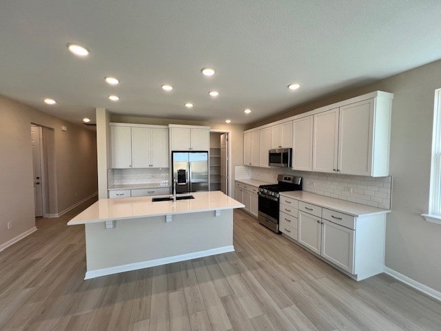 kitchen featuring white cabinets, light wood-type flooring, stainless steel appliances, sink, and a kitchen island with sink