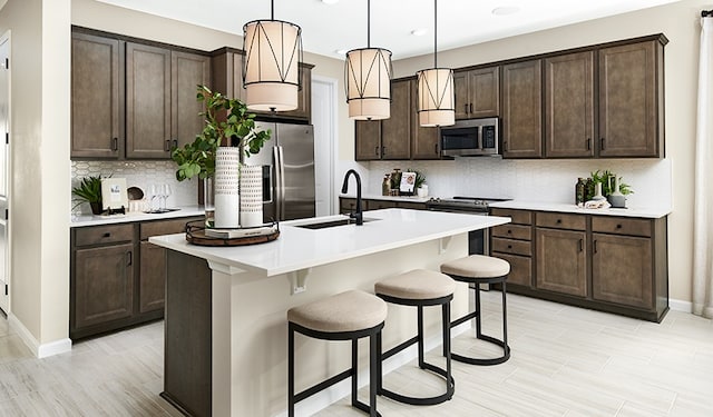 kitchen featuring stainless steel appliances, a center island with sink, a kitchen breakfast bar, and dark brown cabinetry