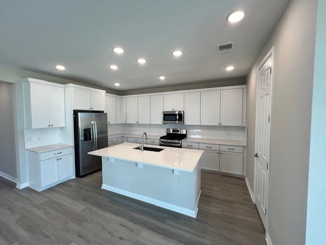 kitchen with dark hardwood / wood-style flooring, appliances with stainless steel finishes, a center island with sink, and white cabinets