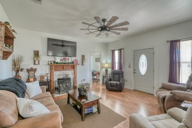 living room with light hardwood / wood-style flooring, ceiling fan, and a stone fireplace