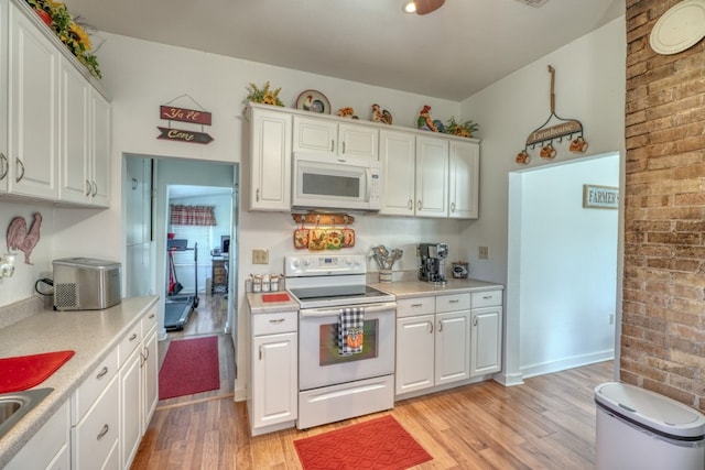 kitchen with white appliances, light hardwood / wood-style flooring, white cabinetry, and brick wall