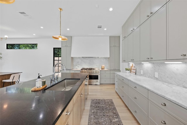 kitchen featuring custom exhaust hood, sink, decorative light fixtures, light hardwood / wood-style flooring, and stainless steel stove