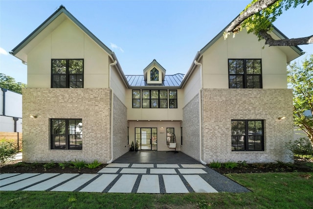 rear view of house featuring a standing seam roof, stucco siding, metal roof, and brick siding