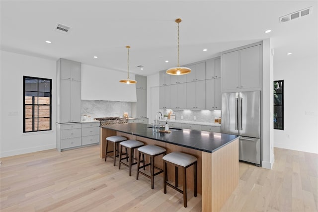 kitchen with a center island with sink, decorative backsplash, light hardwood / wood-style floors, and built in refrigerator