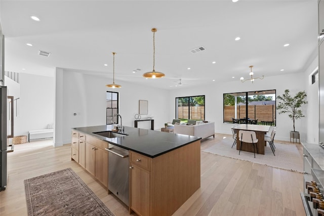 kitchen featuring sink, light wood-type flooring, decorative light fixtures, a center island with sink, and appliances with stainless steel finishes