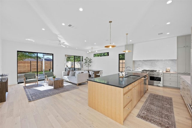 kitchen featuring light brown cabinetry, light wood-type flooring, a spacious island, decorative light fixtures, and high end stainless steel range