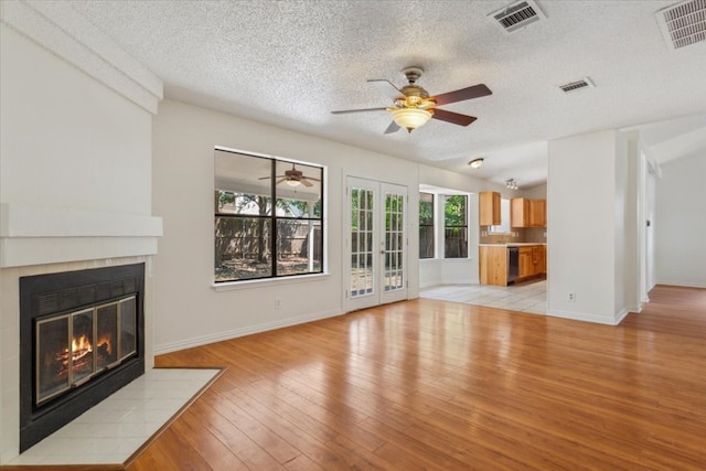 unfurnished living room with a textured ceiling, light wood-type flooring, french doors, and a tiled fireplace