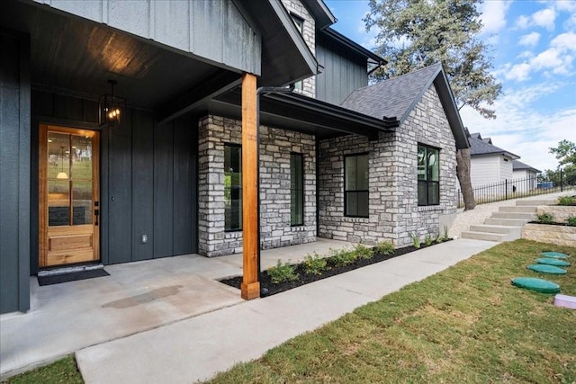 exterior space with a lawn, board and batten siding, roof with shingles, and stone siding
