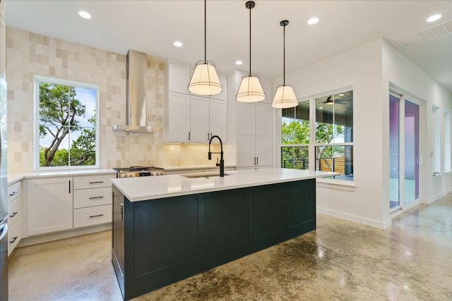 kitchen featuring wall chimney exhaust hood, white cabinetry, a kitchen island with sink, and sink