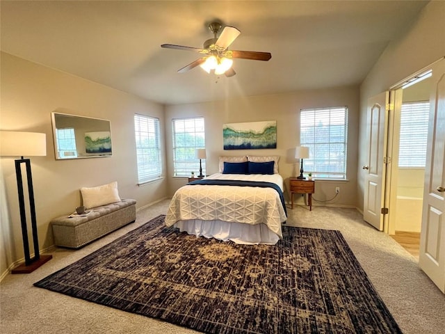 bedroom featuring ceiling fan, ensuite bath, light carpet, and multiple windows