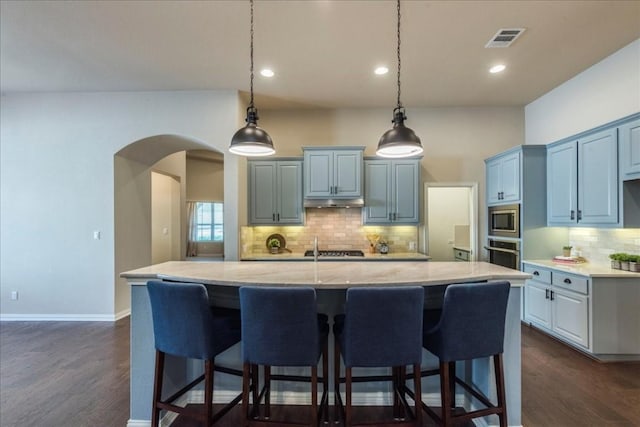 kitchen with arched walkways, appliances with stainless steel finishes, dark wood-type flooring, and light stone countertops