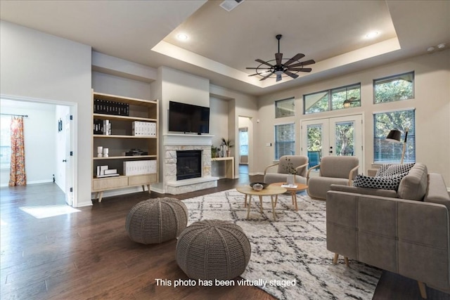 living area featuring a fireplace, wood finished floors, a ceiling fan, french doors, and a raised ceiling