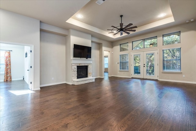 unfurnished living room featuring a stone fireplace, dark wood-type flooring, a raised ceiling, and a ceiling fan