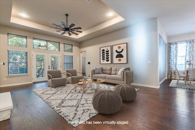 living room with dark wood-type flooring, a raised ceiling, and french doors