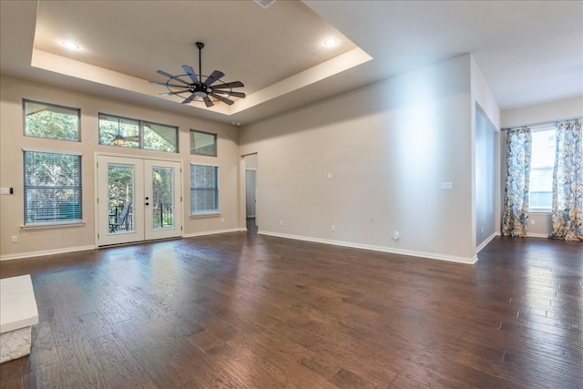 unfurnished living room with a raised ceiling, dark wood finished floors, and french doors