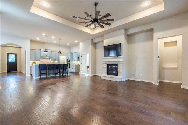 unfurnished living room featuring arched walkways, a stone fireplace, visible vents, dark wood-style floors, and a raised ceiling