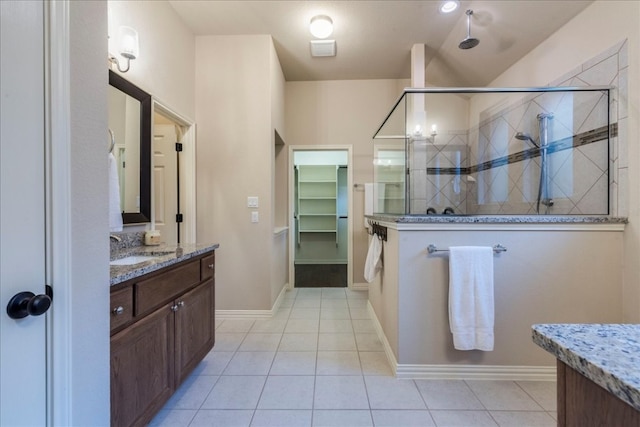 full bathroom with tile patterned flooring, vanity, baseboards, a tile shower, and a walk in closet