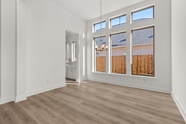 spare room with an inviting chandelier, a towering ceiling, and light hardwood / wood-style flooring