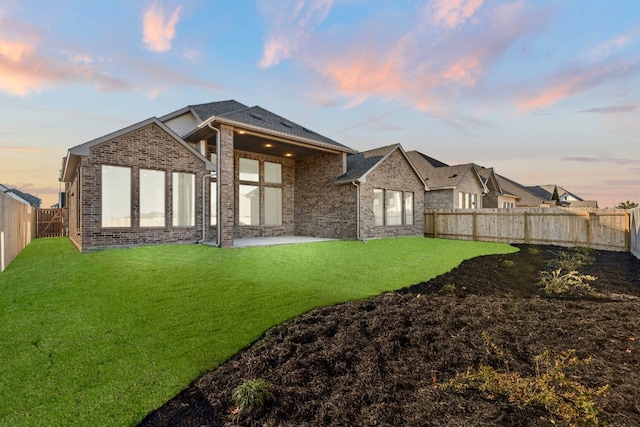 back house at dusk with a patio area and a lawn