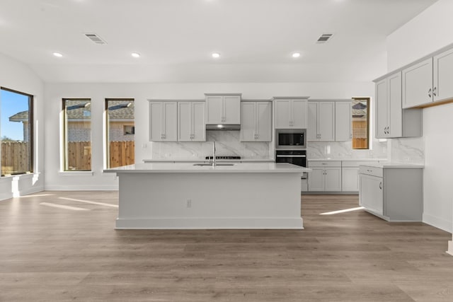 kitchen featuring stainless steel microwave, gray cabinets, oven, and a center island with sink