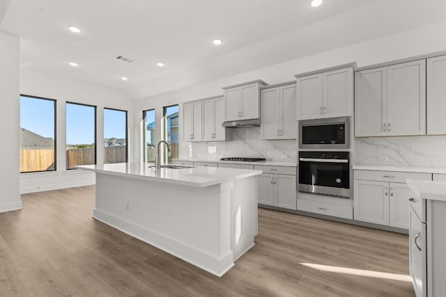 kitchen with stainless steel appliances, an island with sink, sink, and gray cabinetry