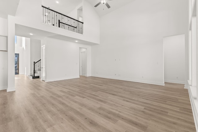 unfurnished living room featuring ceiling fan, a high ceiling, and light wood-type flooring