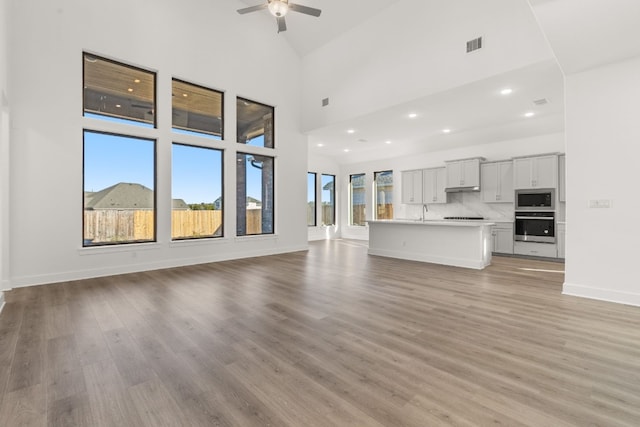 unfurnished living room featuring ceiling fan, high vaulted ceiling, sink, and light hardwood / wood-style floors