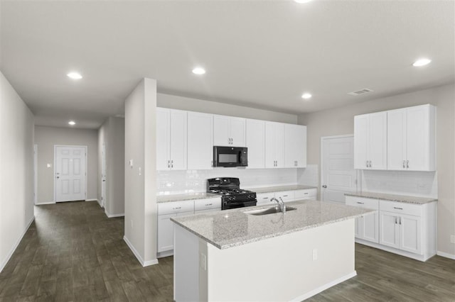 kitchen with an island with sink, dark wood-style floors, a sink, black appliances, and backsplash