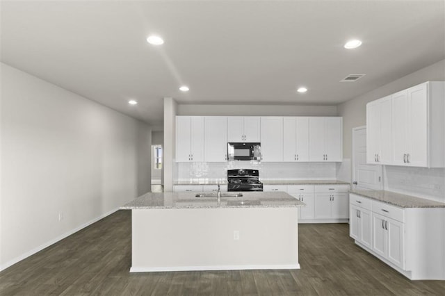 kitchen with range with gas stovetop, black microwave, dark wood-type flooring, and a center island with sink