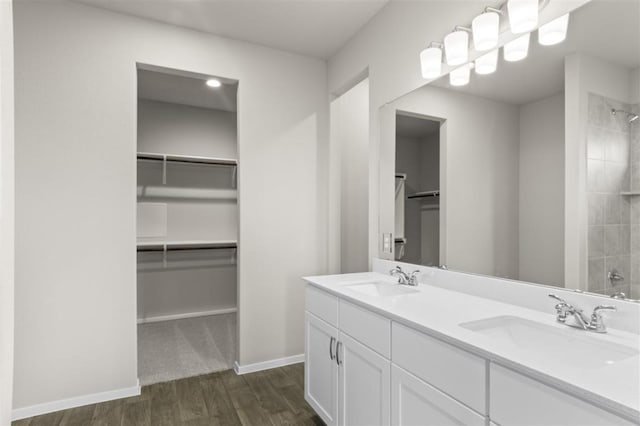 bathroom featuring a spacious closet, wood finished floors, a sink, and tiled shower