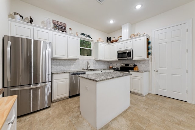 kitchen with stainless steel appliances, a kitchen island, sink, light stone countertops, and white cabinets