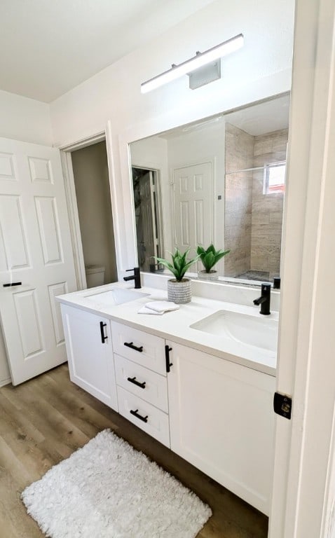 bathroom featuring wood-type flooring, vanity, a tile shower, and toilet