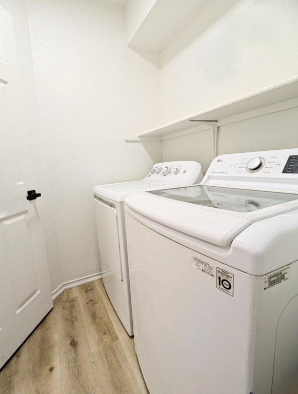 laundry area with washing machine and clothes dryer and light hardwood / wood-style flooring