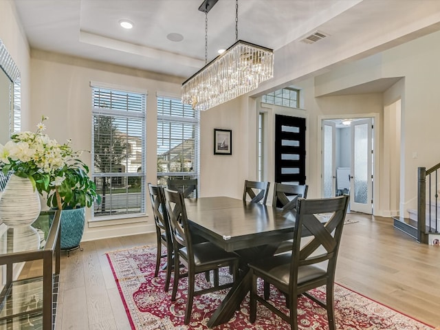 dining area with light wood-type flooring, a tray ceiling, and a notable chandelier