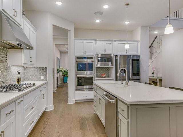 kitchen featuring decorative light fixtures, a center island with sink, tasteful backsplash, light hardwood / wood-style floors, and stainless steel appliances