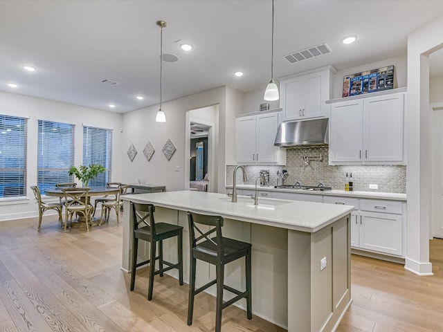 kitchen featuring pendant lighting, light wood-type flooring, white cabinetry, and a kitchen island with sink