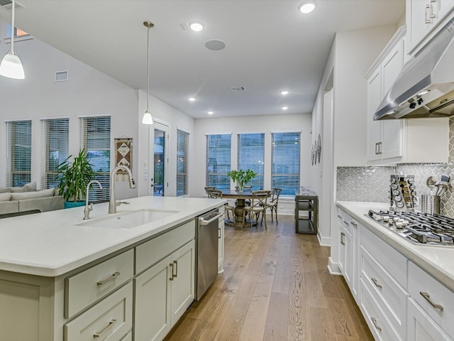 kitchen with light wood-type flooring, appliances with stainless steel finishes, sink, pendant lighting, and a center island with sink