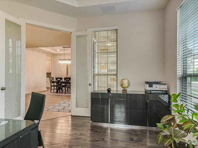 office area with dark wood-type flooring, a raised ceiling, and an inviting chandelier