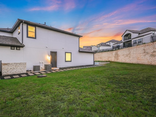 back house at dusk with cooling unit and a lawn