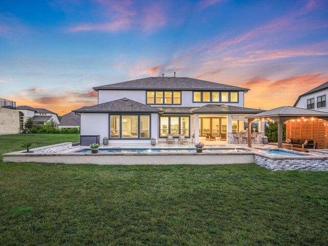 back house at dusk with a lawn and a patio