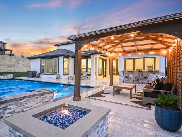 pool at dusk with an outdoor fire pit, an in ground hot tub, and a patio