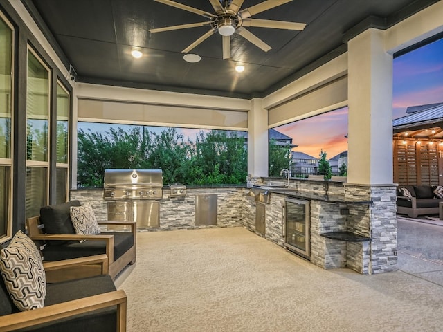 patio terrace at dusk featuring a grill, sink, exterior kitchen, wine cooler, and ceiling fan