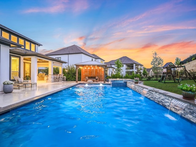 pool at dusk featuring a gazebo, pool water feature, a patio, and a playground